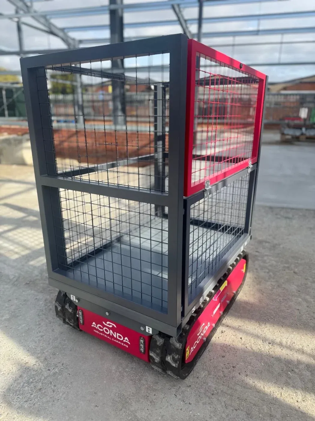 Cage de transport grillagée à armature grise montée sur un transporteur à chenilles Aconda, vue de trois quarts.
