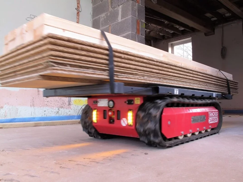 Transporteur à chenilles P'tit Mulet PRO2MAT déplaçant des planches, illustrant l'efficacité du matériel de levage.